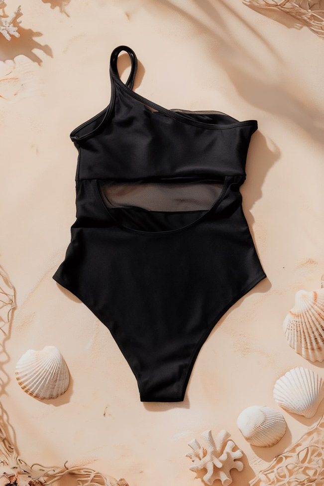 ολόσωμο μαγιό έναν ώμο μαύρο τοποθετημένο σε άμμο με κοχύλια