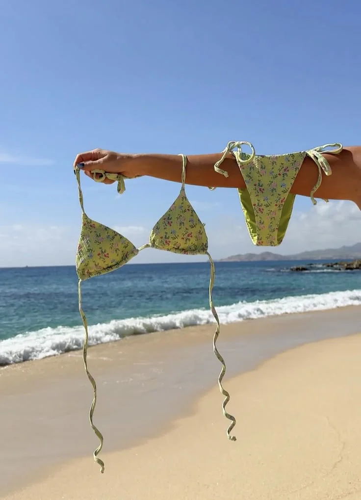 floral μπικίνι σε πράσινη απόχρωση κρατημένο πάνω από την αμμουδιά δίπλα στη θάλασσα
